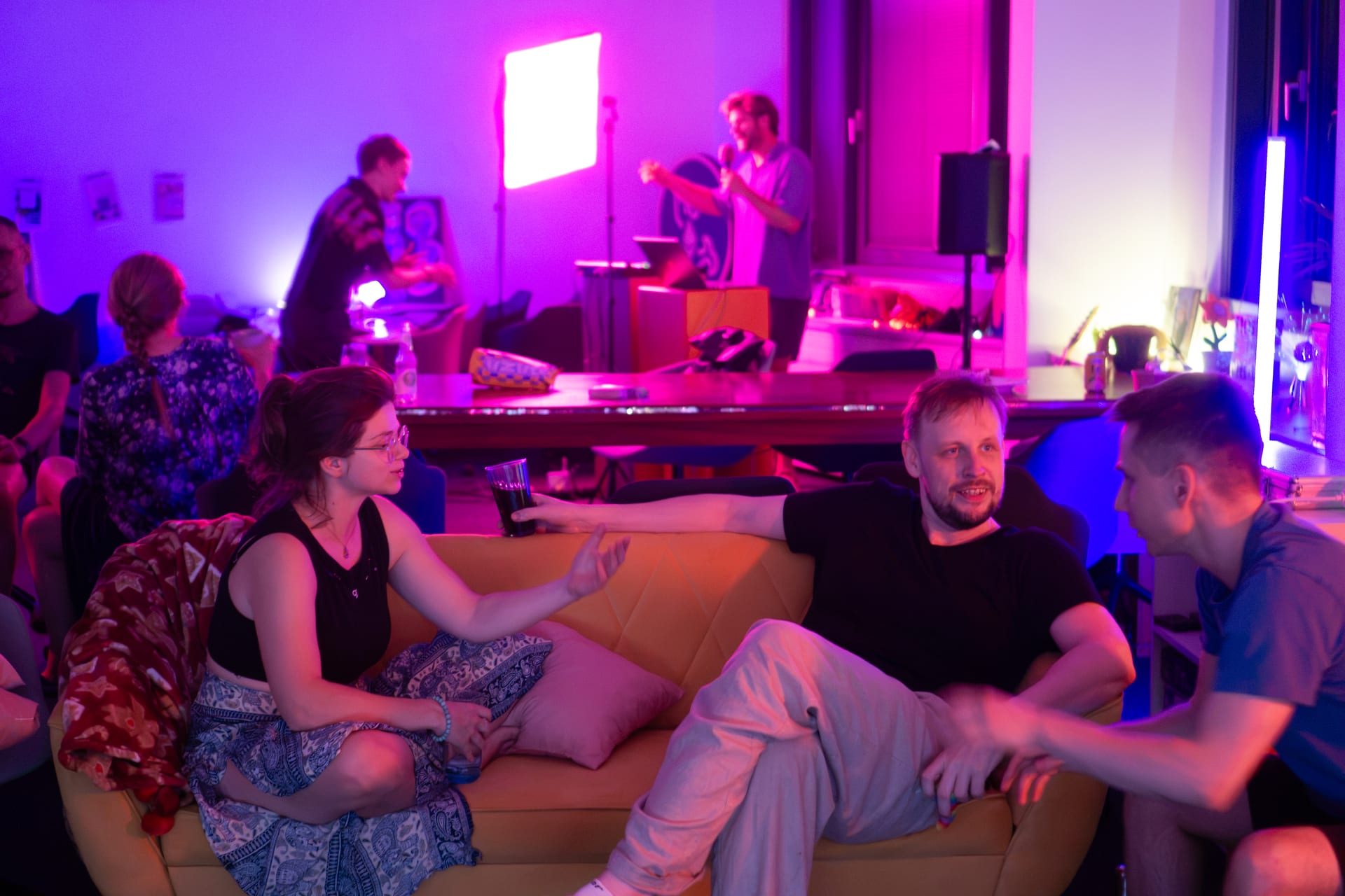 Open mic night, members talking on the sofa while someone performs